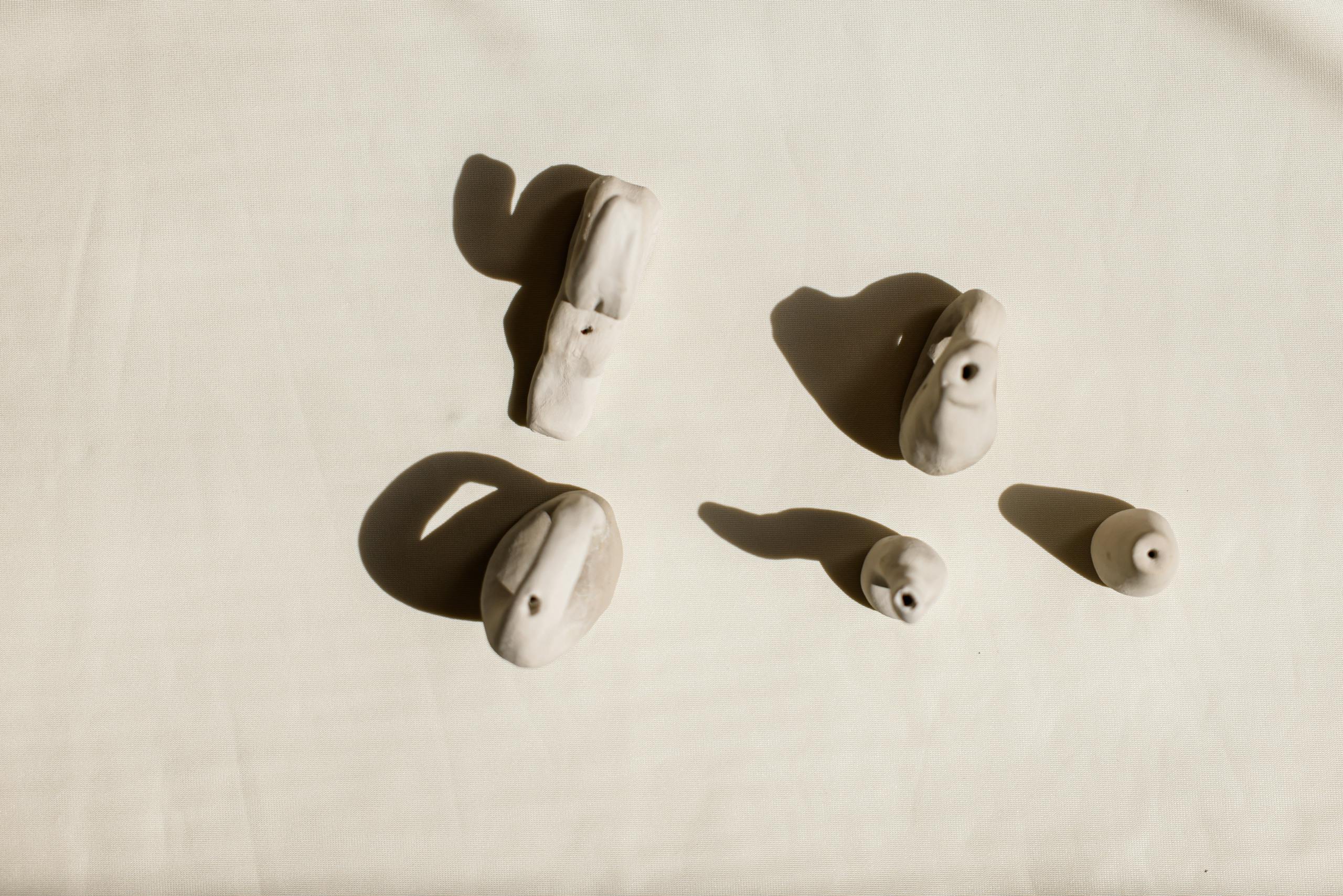 Artistic shot of handmade clay ocarinas on light background, highlighting shadows.